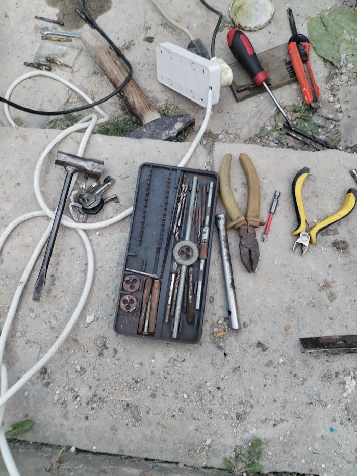 A variety of hand tools laid out for repair work on a concrete floor outdoors in Moldova.